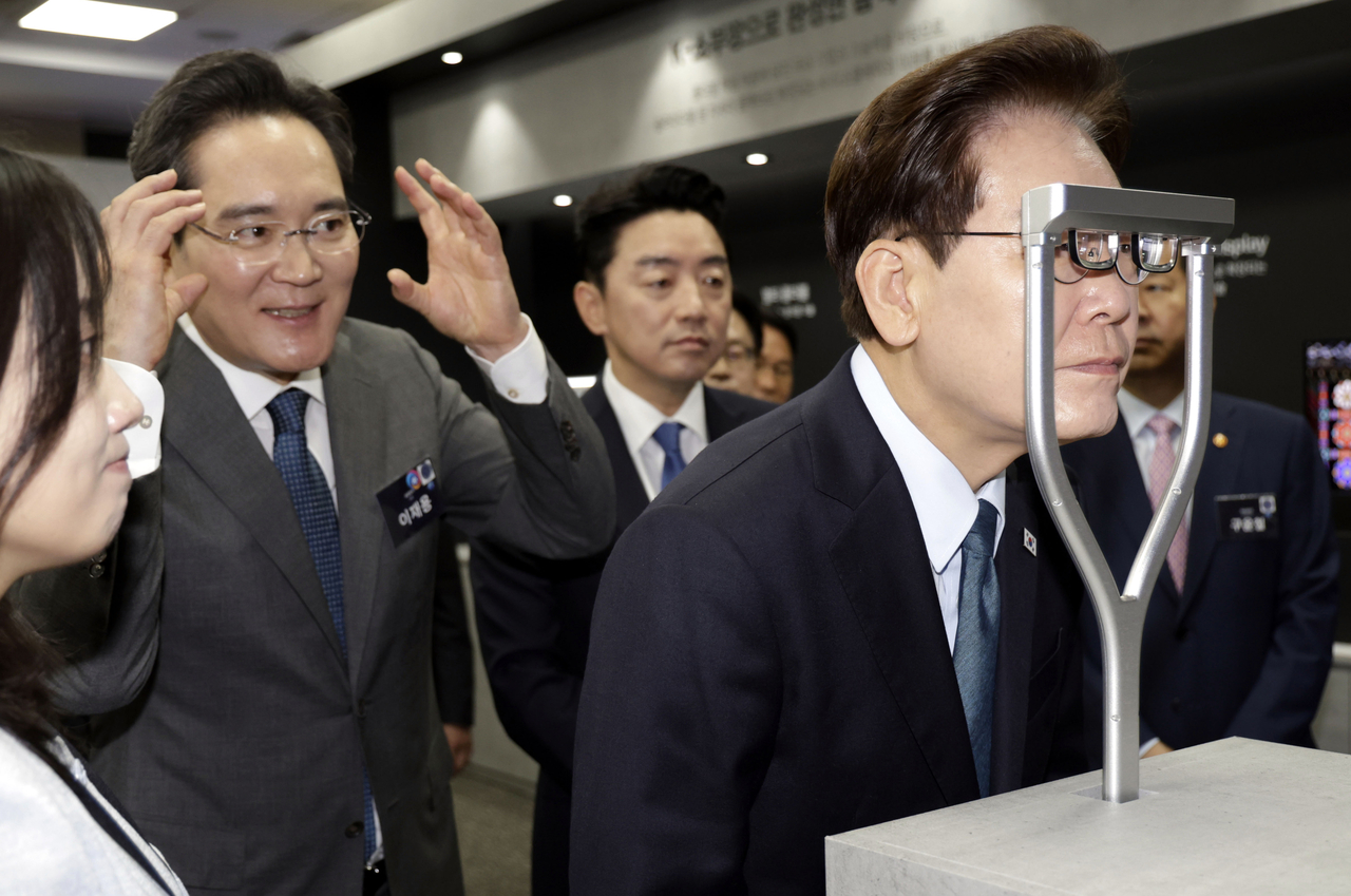 이재명(오른쪽) 대통령이 2일 삼성디스플레이 아산캠퍼스에서 열린 ‘충청권 첨단산업 발전비전 국민보고회’에서 차세대 AR(증강현실) 글래스를 체험하고 있다. 그 뒤에서 이재용(왼쪽) 삼성전자 회장이 AR 글라스에 대한 부연 설명을 하고 있다.  [연합]