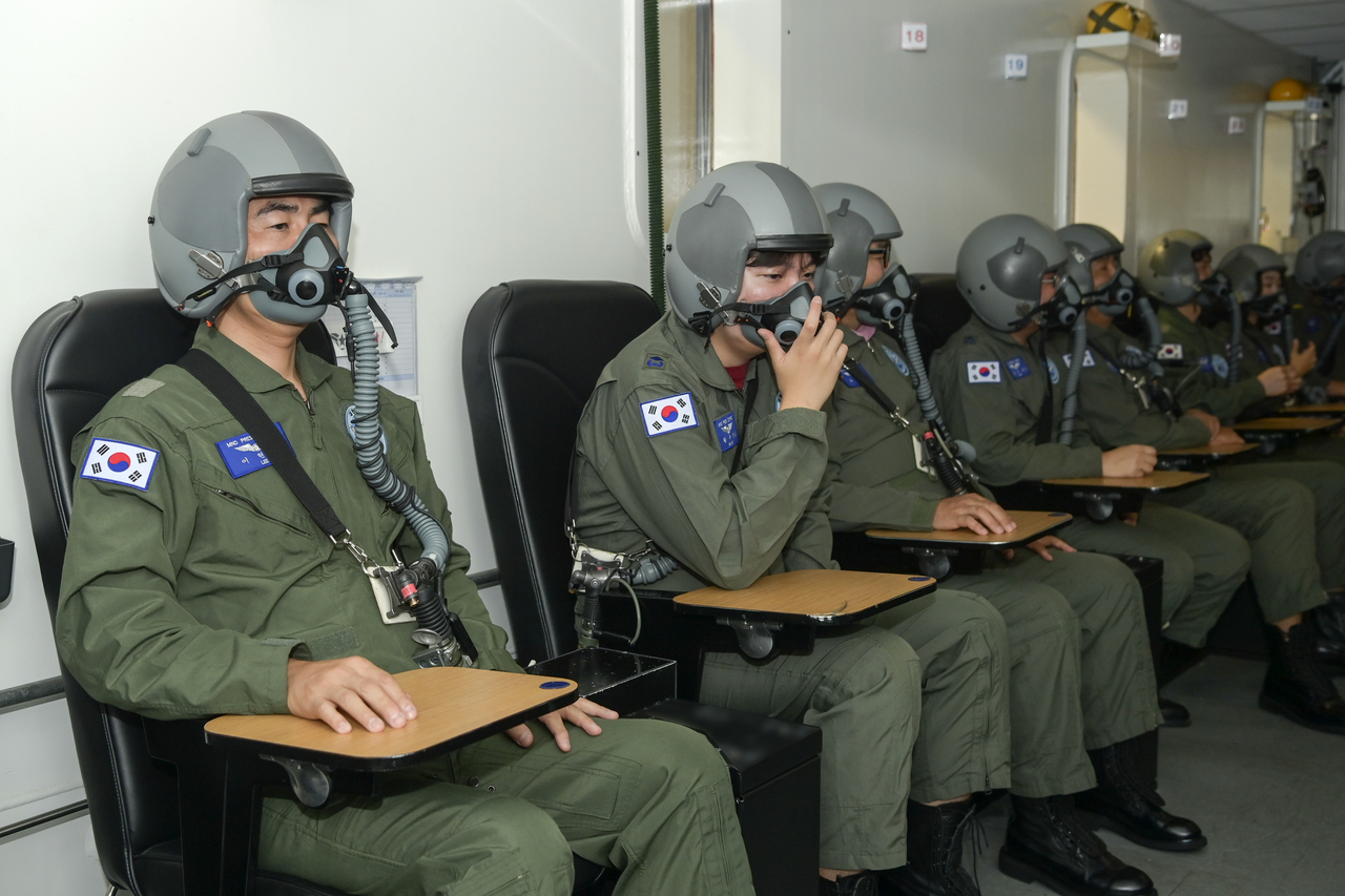 Participants wearing oxygen masks and helmets wait inside an altitude chamber. (Republic of Korea Air Force)