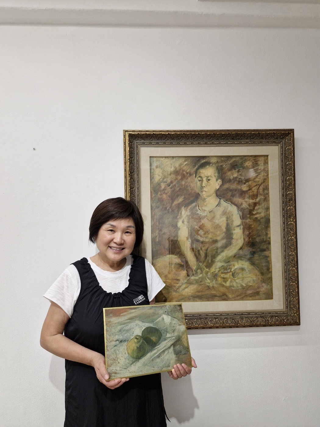 Diana Kang poses holding "Still Life" in front of "Seated Boy" at her home in Seoul in July 2024, the day Kim Jae-seon's paintings arrived. (Courtesy of Diana Kang)