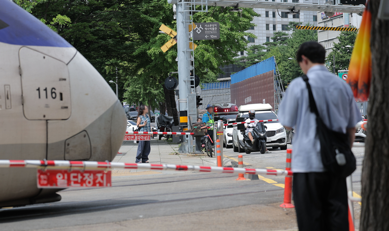 Peopla and cars wait at a railroad crossing beneath the Seosomun overpass in Seoul on Saturday after traffic under the overpass fully reopened following the completion of its demolition. (Yonhap)