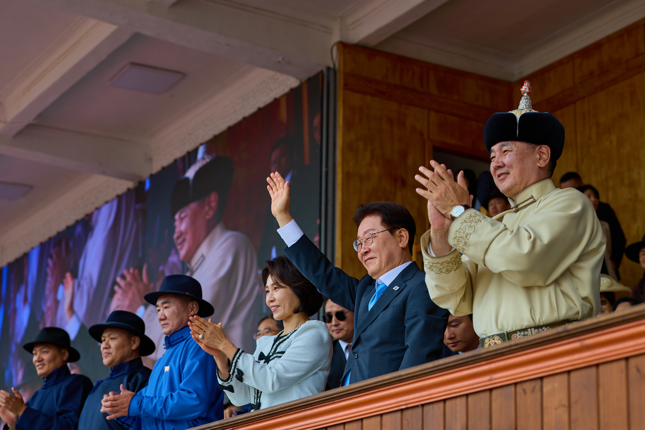 President Lee Jae Myung waves to spectators alongside Mongolian President Ukhnaagiin Khurelsukh during the opening ceremony of the Naadam Festival at the National Sports Stadium in Ulaanbaatar, Mongolia, on Saturday. First lady Kim Hye Kyung is seen to Lee's left. (Pool photo via Yonhap)