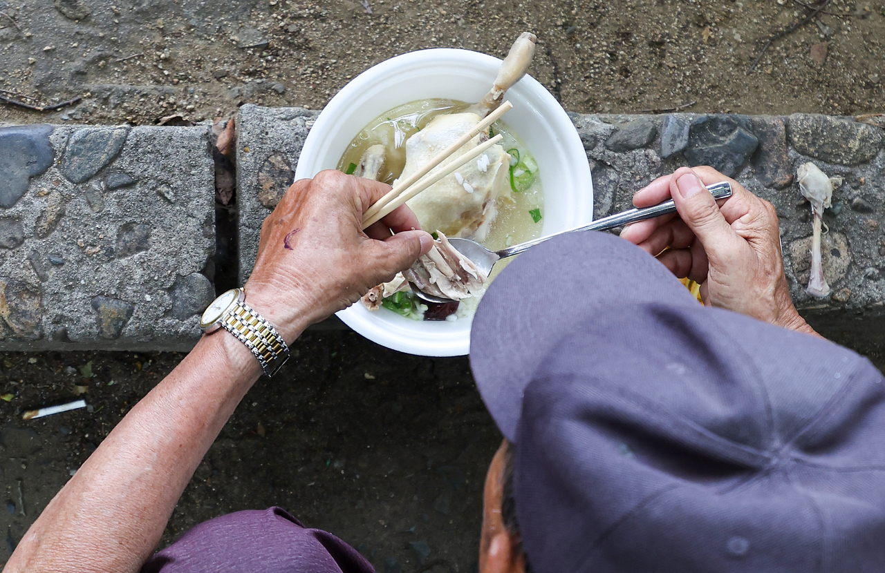 A senior citizen eats a free bowl of samgyetang served at Duryu Park in Daegu on the day before chobok, part of a Korean community stamina food sharing tradition