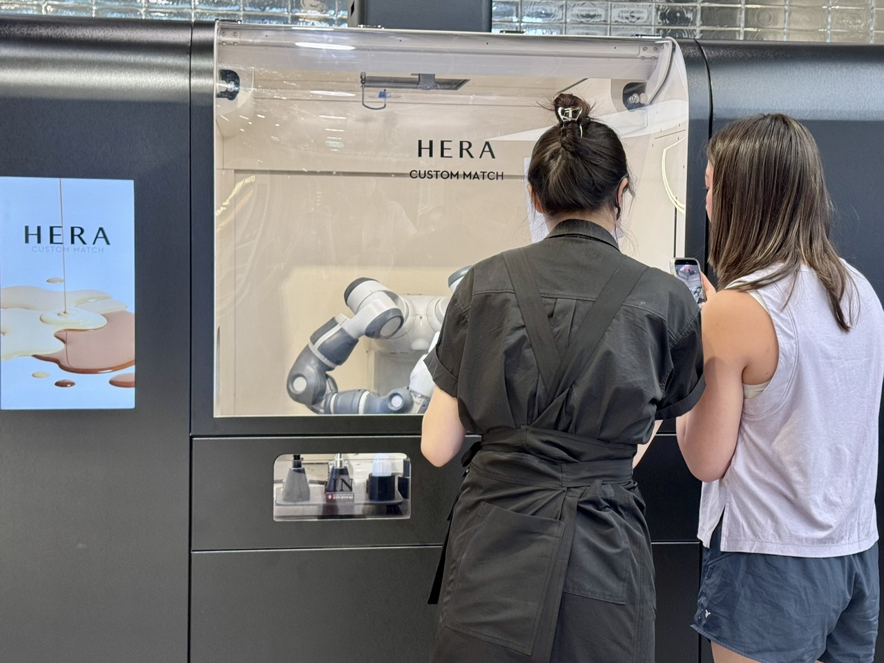A beauty consultant assists a customer while a robotic system prepares a custom Hera foundation at Amore Yongsan on Thursday. (No Kyung-min/The Korea Herald)