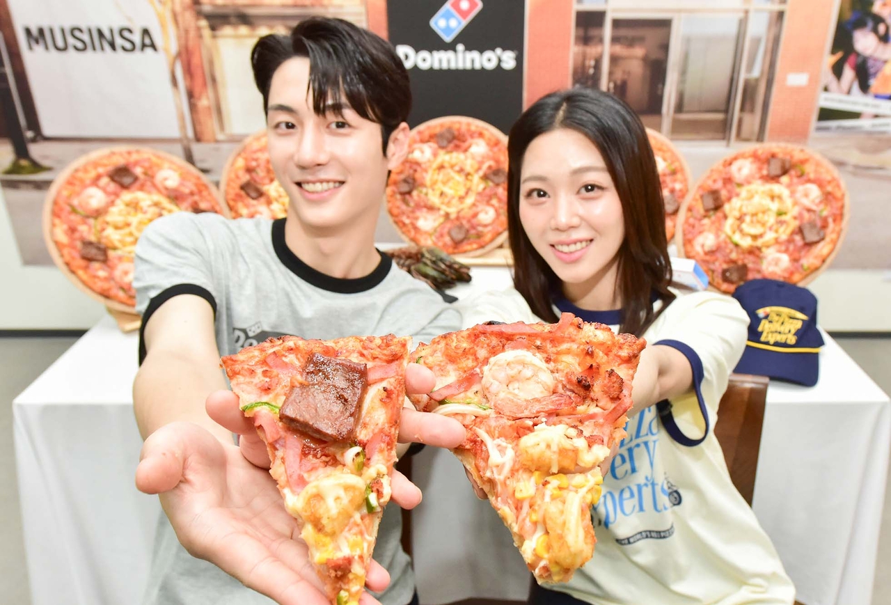 14일 모델들이 도미노피자와 국내 대표 패션·뷰티 스토어 무신사가 협업한 ‘무진장 슈림프 스테이크 피자’를 소개하고 있다. [사진=도미노피자]