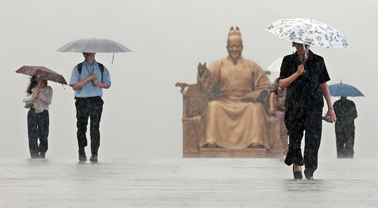 Pedestrians cross a street near Gwanghwamun Station in central Seoul on July 14 as heavy rain falls. (Yonhap)