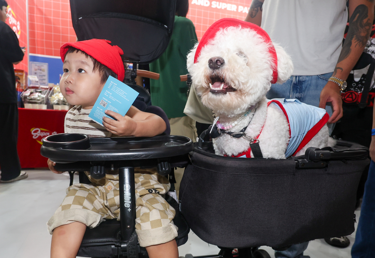 A child sits beside a dog wearing a matching red cap at K-Pet Fair Seoul on Friday. (Newsis)