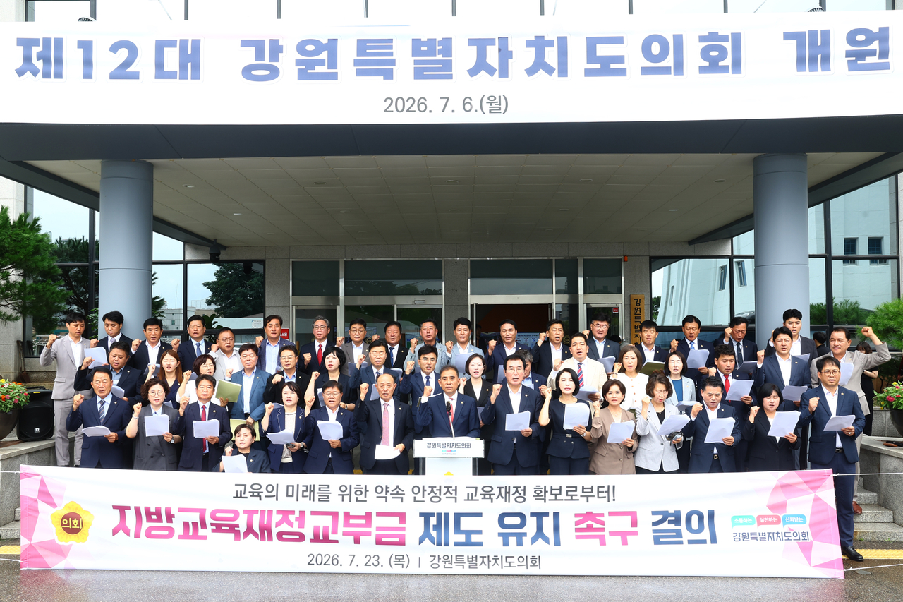 강원도의회 여야의원들이 모두 의회 현관에 모여, 학령인구 감소를 이유로 지방교육제정교부금을 줄이려는 중앙정부의 최근 움직임에 대해 비판하며 현행 유지를 촉구하고 있다.