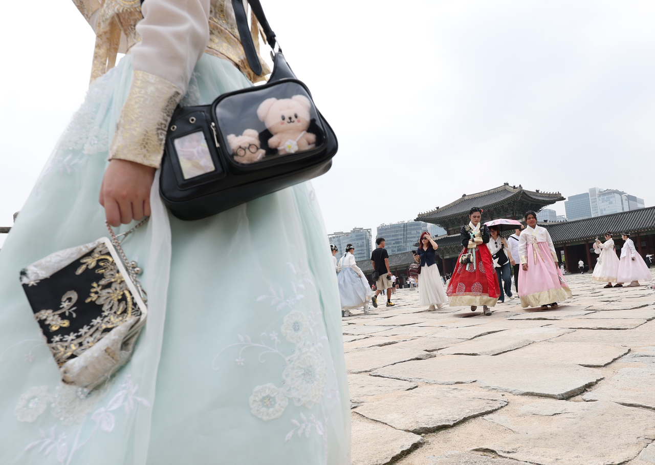 A visitor to Gyeongbokgung in Seoul carries a bag with K-pop merchandise while wearing Korea's traditional hanbok on July 16. (Yonhap)