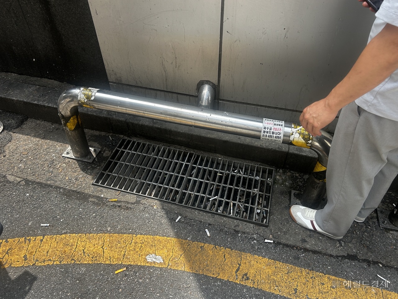 A storm drain near Gangnam Station filled with cigarette butts, Friday afternoon. A smoker stands nearby. (Lee Jun-young/The Herald Business)