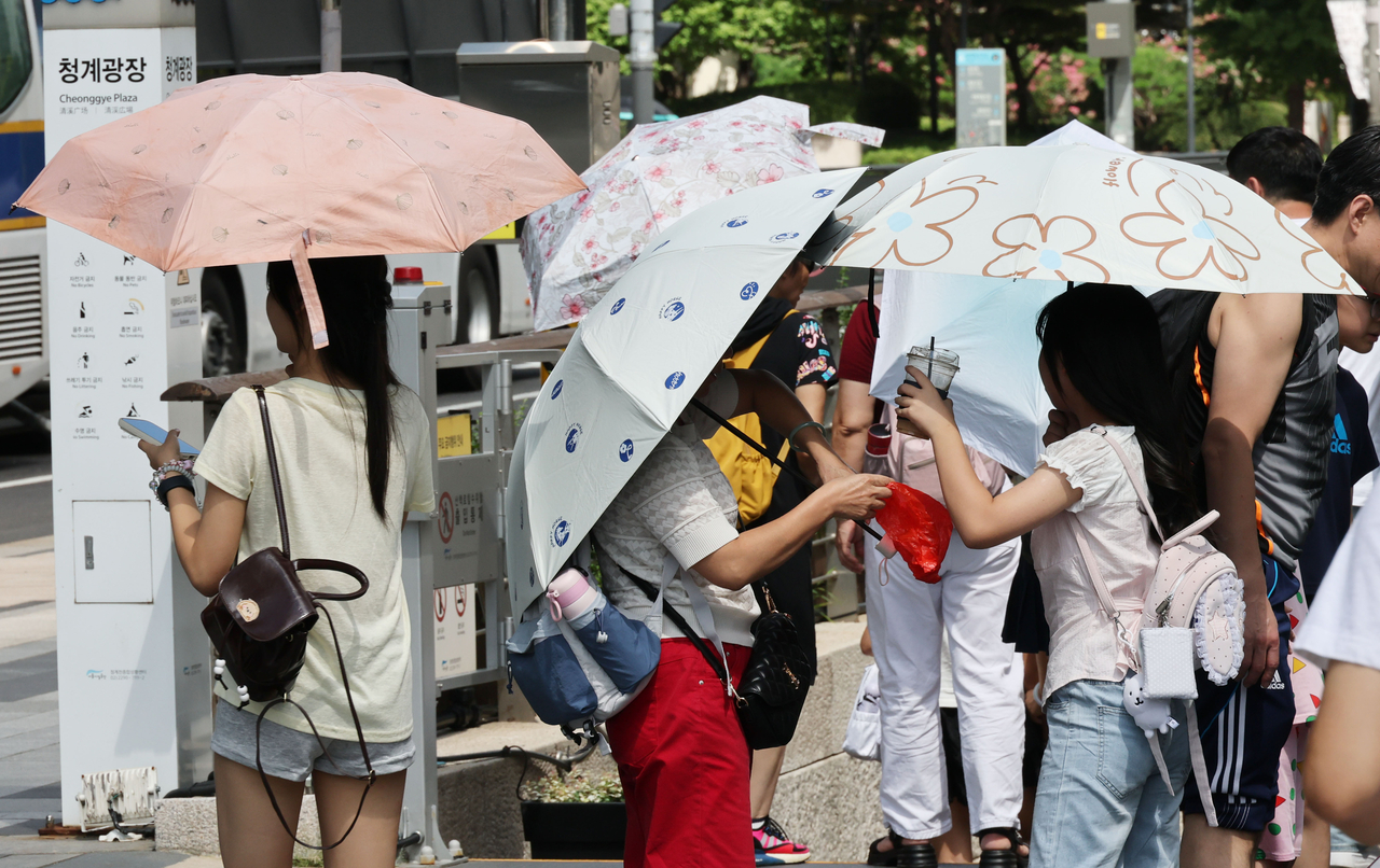 서울 전역에 폭염주의보가 발효된 26일 서울 청계천에서 시민들이 양산을 쓰고 이동하고 있다. [연합]