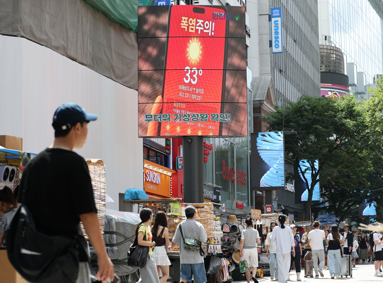 Seoul citizens walk past a notification that says a heat wave warning has been issued in Myeong-dong on Sunday. (Yonhap)