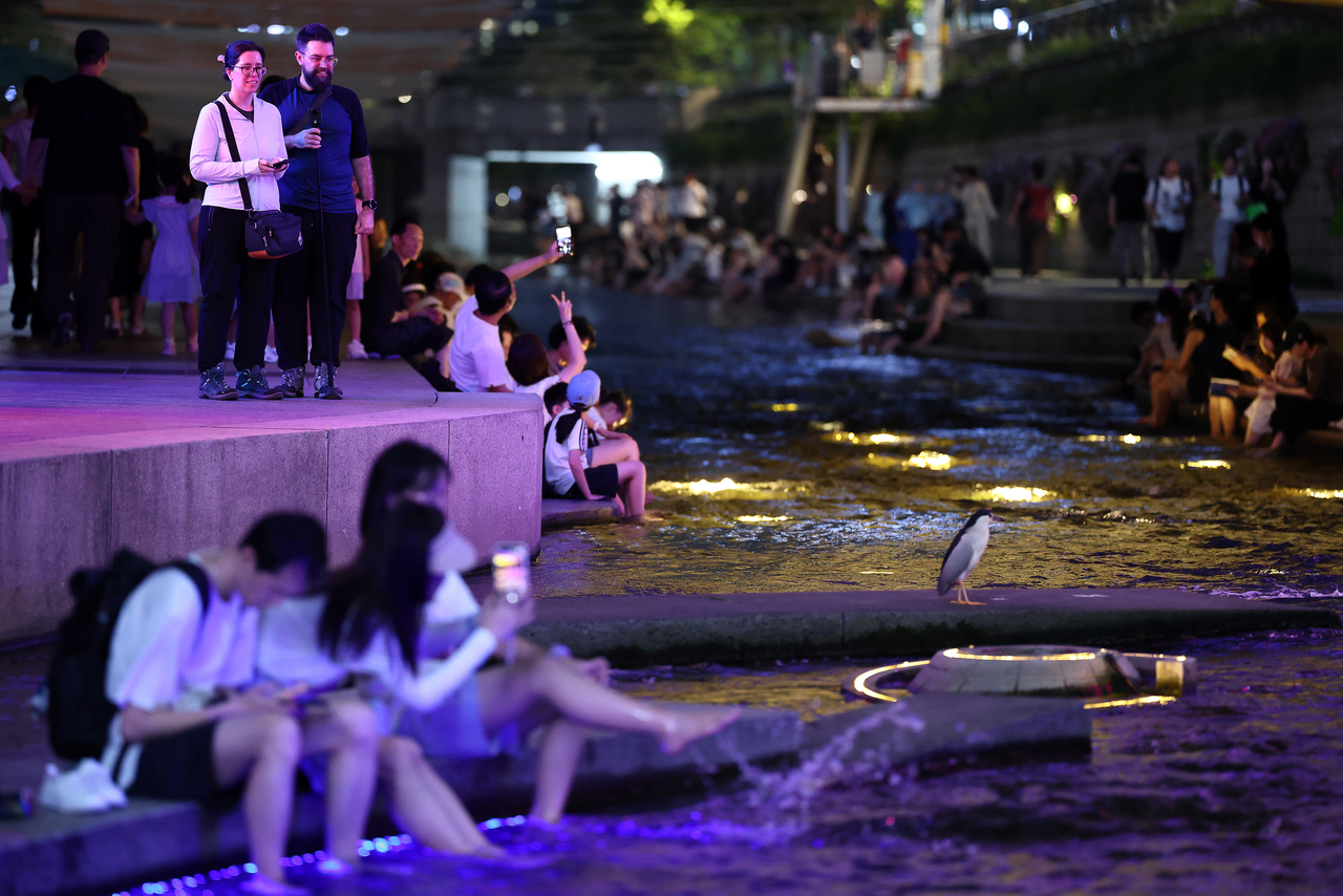 People cool off along the Cheonggye Stream in central Seoul as a tropical night advisory is in effect across most parts of the nation on Monday. (Yonhap)