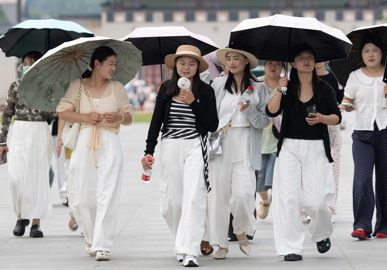Tourists visiting Gyeongbokgung in central Seoul use parasols to shield themselves from the heat on Wednesday afternoon. (Yoon Chang-bin/The Korea Herald)