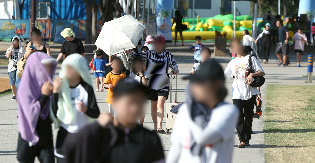 경남 양산지역 낮 최고기온이 40.3도까지 치솟은 29일 오후 양산시 물금읍 운영이 종료된 황산공원 물놀이장을 나서는 피서객들이 모자와 양산으로 뜨거운 햇빛을 가리고 있다. [연합]