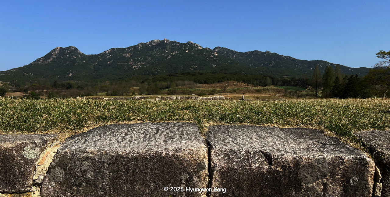 Songaksan mountain, rising behind Manwoldae in Kaesong, North Korea, has long been imagined as the figure of a reclining woman gazing toward the sky. In traditional geomancy, its western ridge forms her head, the central peaks her breasts, and the eastern ridge her outstretched legs. Manwoldae, the principal imperial palace of the Goryeo empire, was built just below the figure’s breast, symbolically drawing upon the life-giving energy of the mountain goddess. (Hyungwon Kang)