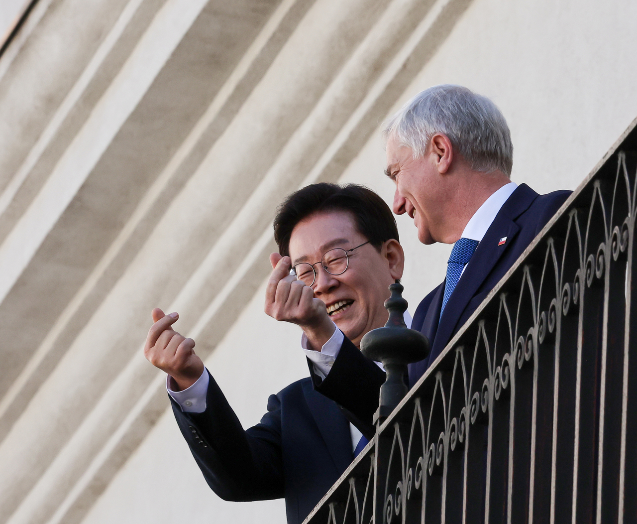 President Lee Jae Myung and Chilean President Jose Antonio Kast make finger-heart gestures toward members of their delegations and reporters as they enter La Moneda Palace in Santiago after an official welcoming ceremony on Thursday. (Yonhap)