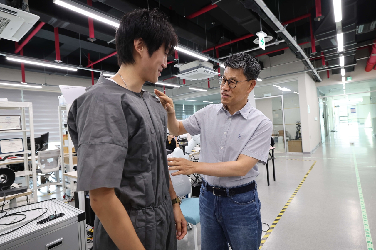 Ryu Jee-hwan (right), professor at the Korea Advanced Institute of Science and Technology's Department of Civil and Environmental Engineering, examines a self-dressing robot at KAIST in Daejeon on Monday. (KAIST)