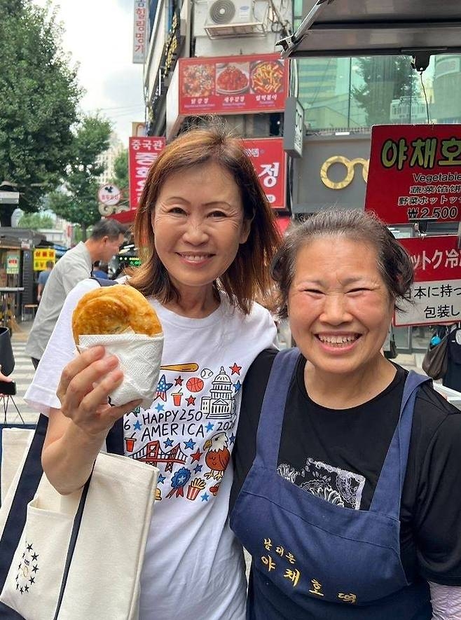 US Ambassador to South Korea Michelle Steel (left) poses for a photo with a vendor at a traditional Korean market in central Seoul while holding hotteok, a Korean pancake, in this photo uploaded to her X account on Saturday. (Screenshot from Michelle Steel's X account)