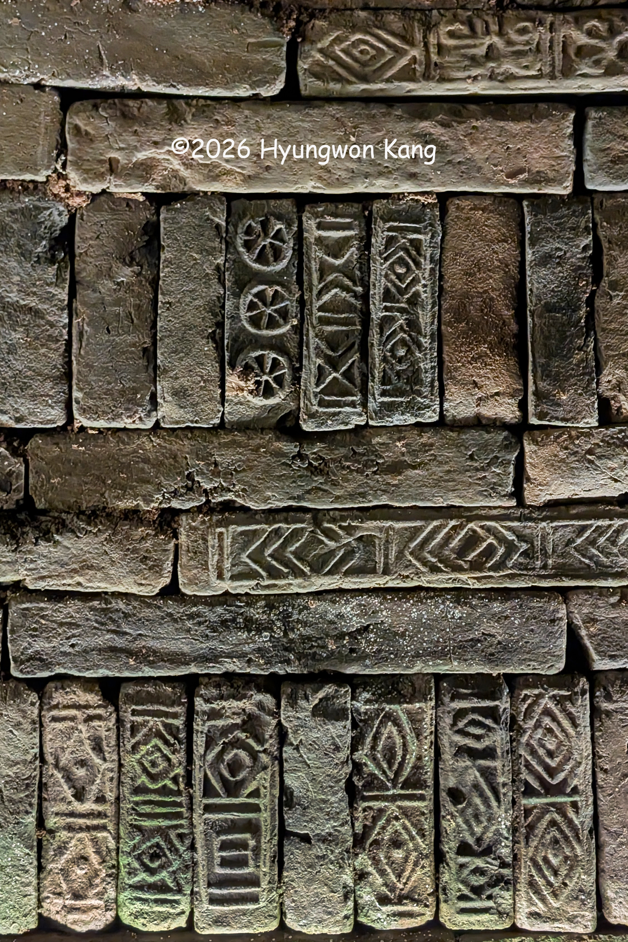 A close-up view shows a brick chamber wall at the Rangnangguk Museum in Pyongyang, with a distinctive pattern of three horizontal courses of flat bricks alternating with one vertical course. Many of the bricks bear geometric and symbolic designs reminiscent of Korean petroglyphs and traditional decorative motifs. (Hyungwon Kang)