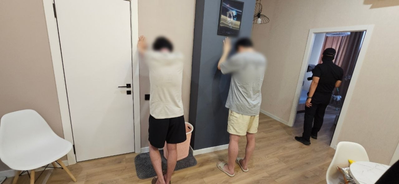 Two suspected scam ring members stand with their arms against the wall as Korean and Kazakh law enforcement raid a safe house in Almaty, Kazakhstan, on July 23. (National Police Agency).