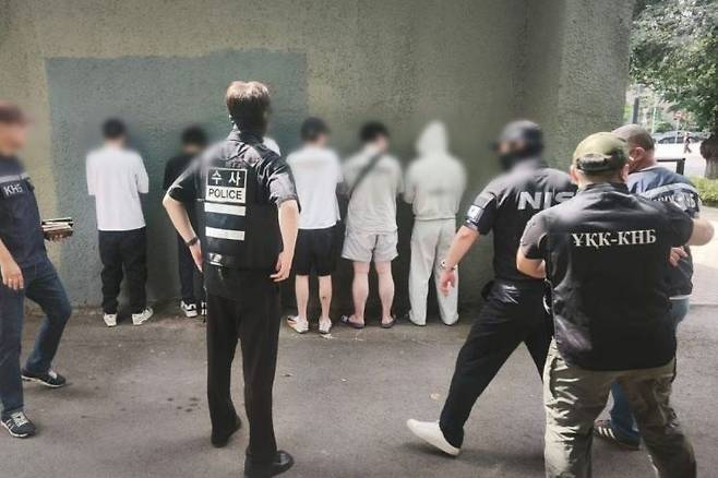 Suspected scam ring members stand facing a wall as Korean and Kazakh law enforcement officers raid a safe house in Almaty, Kazakhstan, on July 23. (National Police Agency)