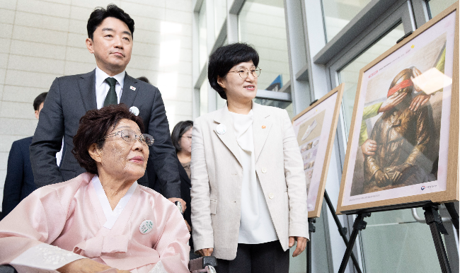 Lee Yong-soo (seated), a survivor of Japan's wartime sexual slavery, takes a look at a winning entry of the youth contest on sexual slavery victims, with the Minister of Gender Equality and Family Won Min-kyong (right) and Chief of Staff to the President Kang Hoon-sik on Friday. (Yoon Chang-bin/The Korea Herald)