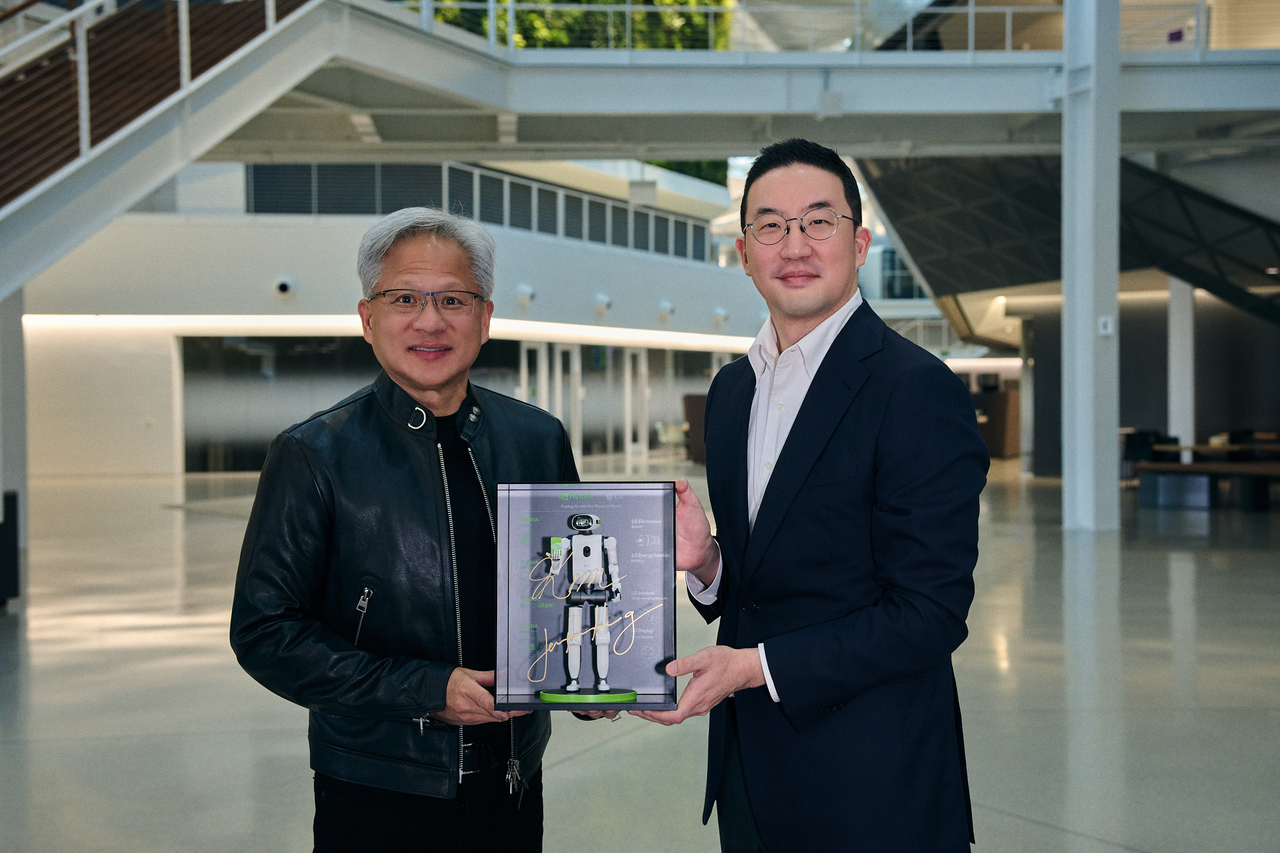 LG Group Chairman Koo Kwang-mo (right) and Nvidia CEO Jensen Huang pose with a miniature humanoid robot after signing a partnership agreement at Nvidia's headquarters in Santa Clara, California, Thursday. The robot, presented by LG as a gift, bears the signatures of Koo and Huang. (LG Corp.)