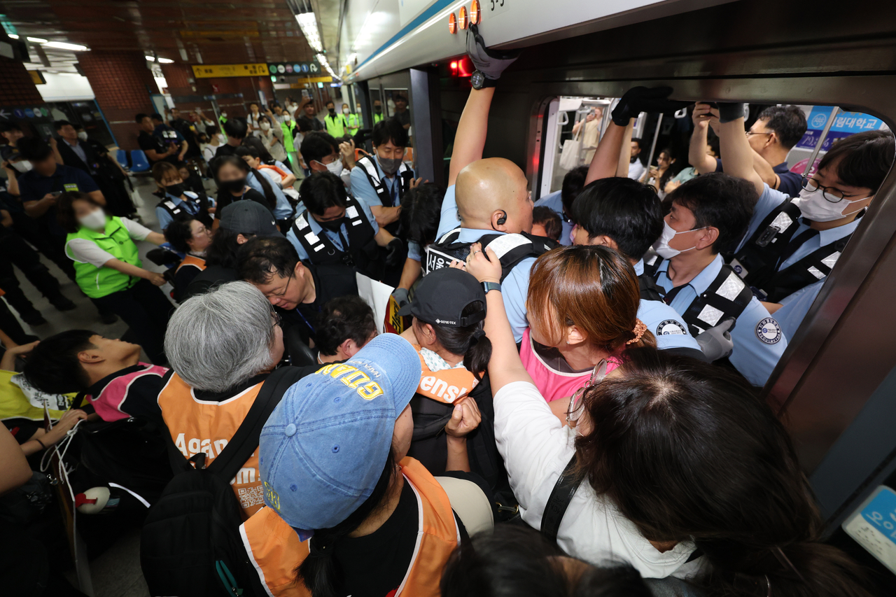 Activists from the Solidarity Against Disability Discrimination clash with officials while holding a subway boarding protest on the platform of Seoul Station on Tuesday. (Yonhap)