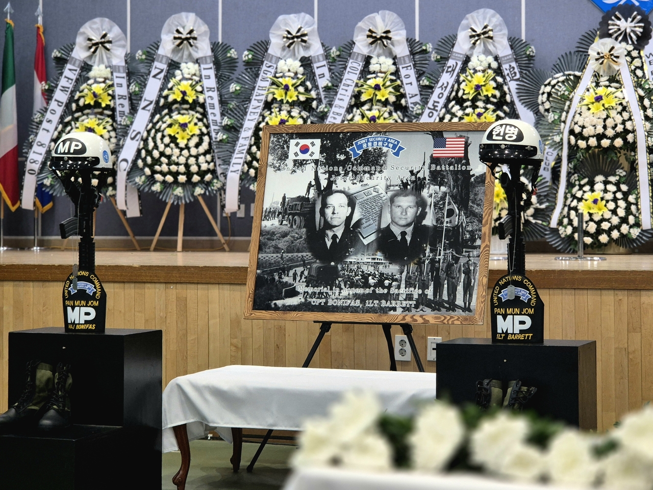 A ceremony marking the 50th anniversary of the 1976 Panmunjom axe murder, in which North Korean soldiers attacked and killed two US Army officers, is held Tuesday at Park Gym in the Joint Security Area in Gyeonggi Province. Portraits of Maj. Arthur Bonifas and 1st Lt. Mark Barrett are displayed in front of memorial flowers alongside their combat boots and helmets. (Joint Press Corps)