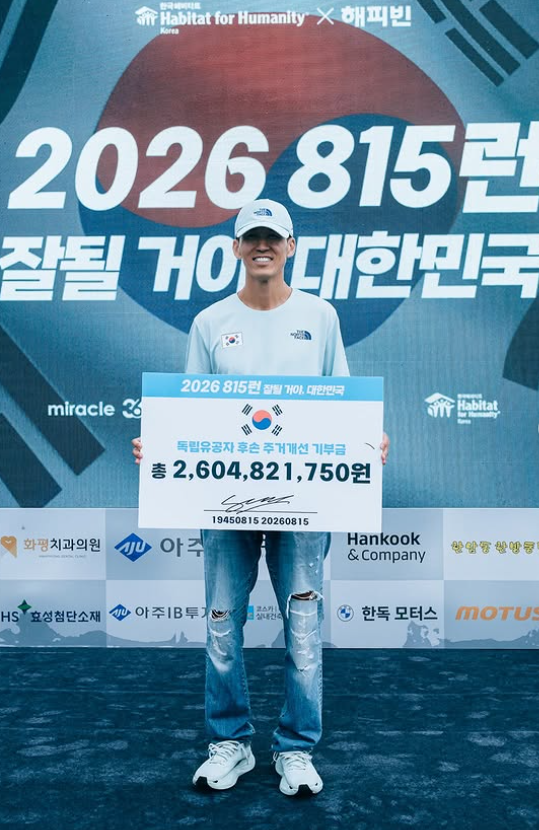 Sean holds a placard showing the 2.6 billion won donated to Habitat for Humanity through this year's 815 Run, with many corporations contributing. (@jinusean3000)