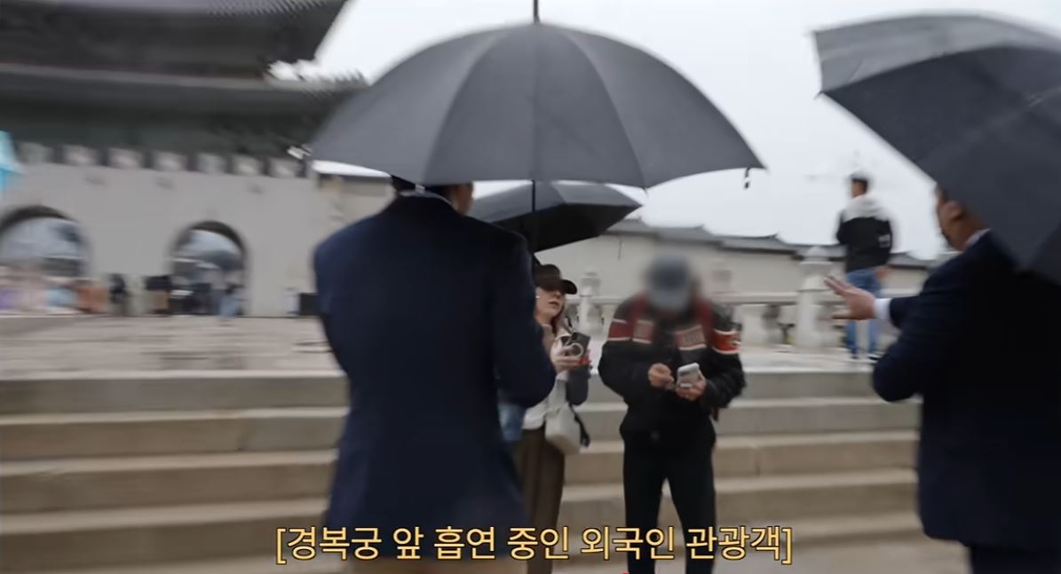 In a screenshot from a video uploaded to Choi Si-won's YouTube channel on Aug. 18, Choi (left) asks a foreign tourist to stop smoking near Gyeongbokgung in Seoul. (Choi Si-won's YouTube channel)
