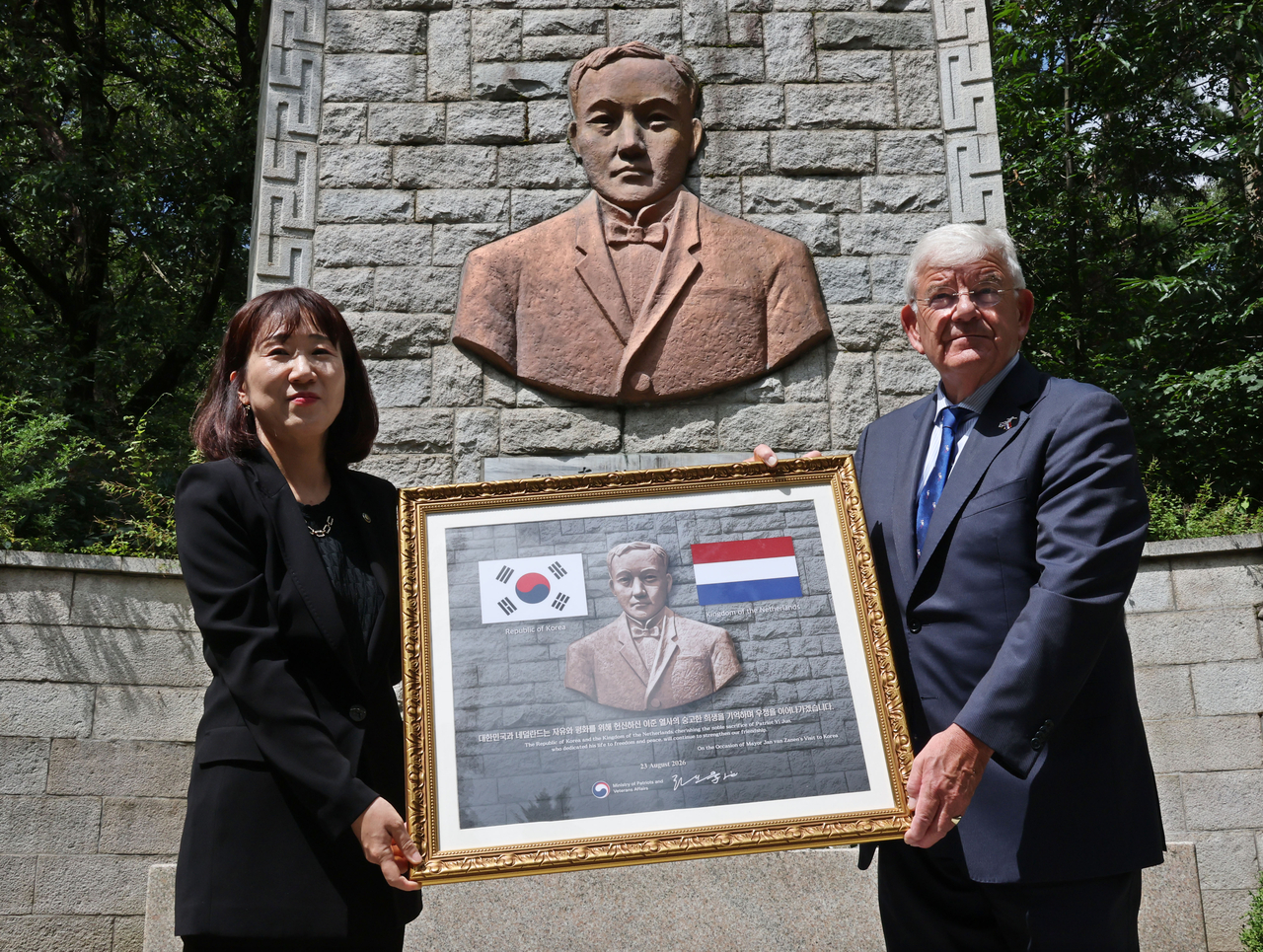 Kang Yunjin (left), vice minister of patriots and veterans affairs, hands a commemorative plaque to the Jan van Zanen, mayor of The Hague, Netherlands, in front of the tomb of Korean independence activist Yi Jun, in Seoul on Sunday. (Yonhap)