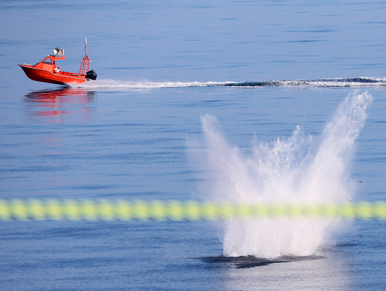 A suicide drone falls into the sea as an orange uncrewed surface vessel, serving as a simulated enemy target, passes in front of it during a test off Busan on Tuesday. (Joint Press Corps via Yonhap)