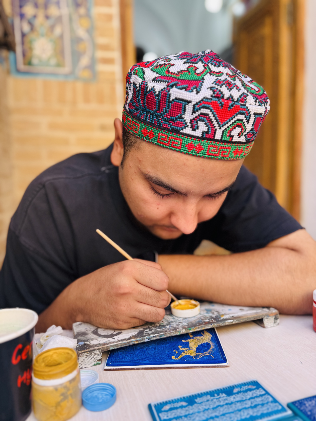 An Uzbek artist wearing a brightly embroidered traditional skullcap (doppa) works on traditional artwork at the historic Shah-i-Zinda funerary complex in Samarkand, Uzbekistan, showcasing the country’s rich tradition of decorative arts. (Sanjay Kumar/The Korea Herald)