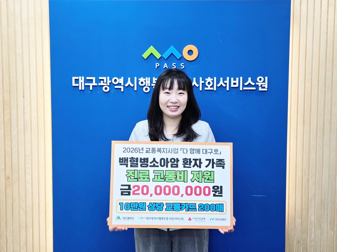 Jung Ha-jin, head of the community services team at the Daegu Happiness Foundation, holds a commemorative placard marking the distribution of 200 transportation cards — each worth 100,000 won ($73) — to families of leukemia and childhood cancer patients, totaling 20 million won.