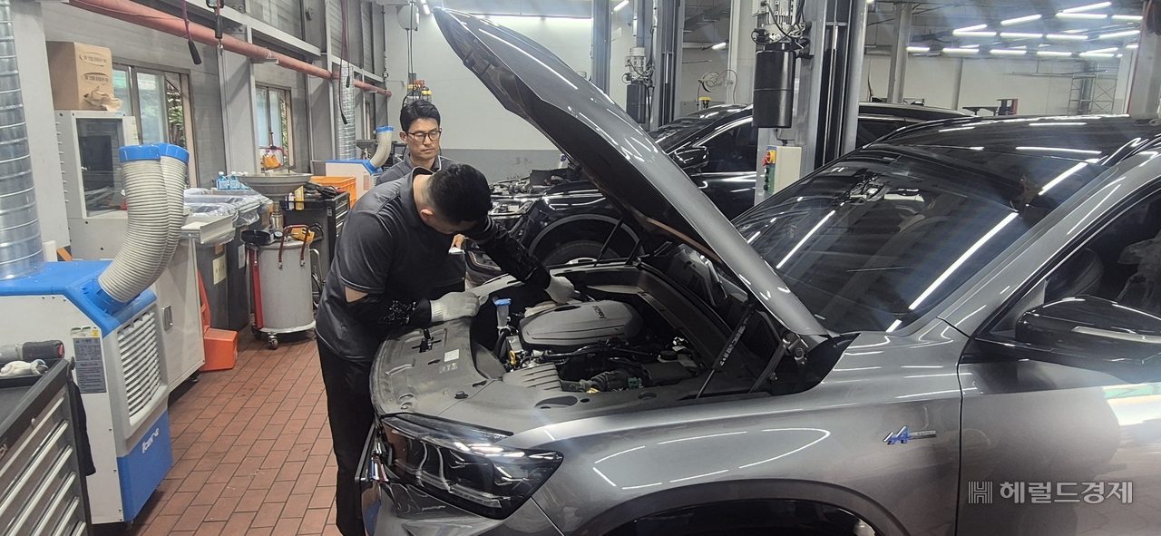 A technician inspects the engine compartment of a vehicle at Renault Korea's Changwon Central Service Center. The facility handles routine maintenance, warranty repairs, and accident and insurance repairs.