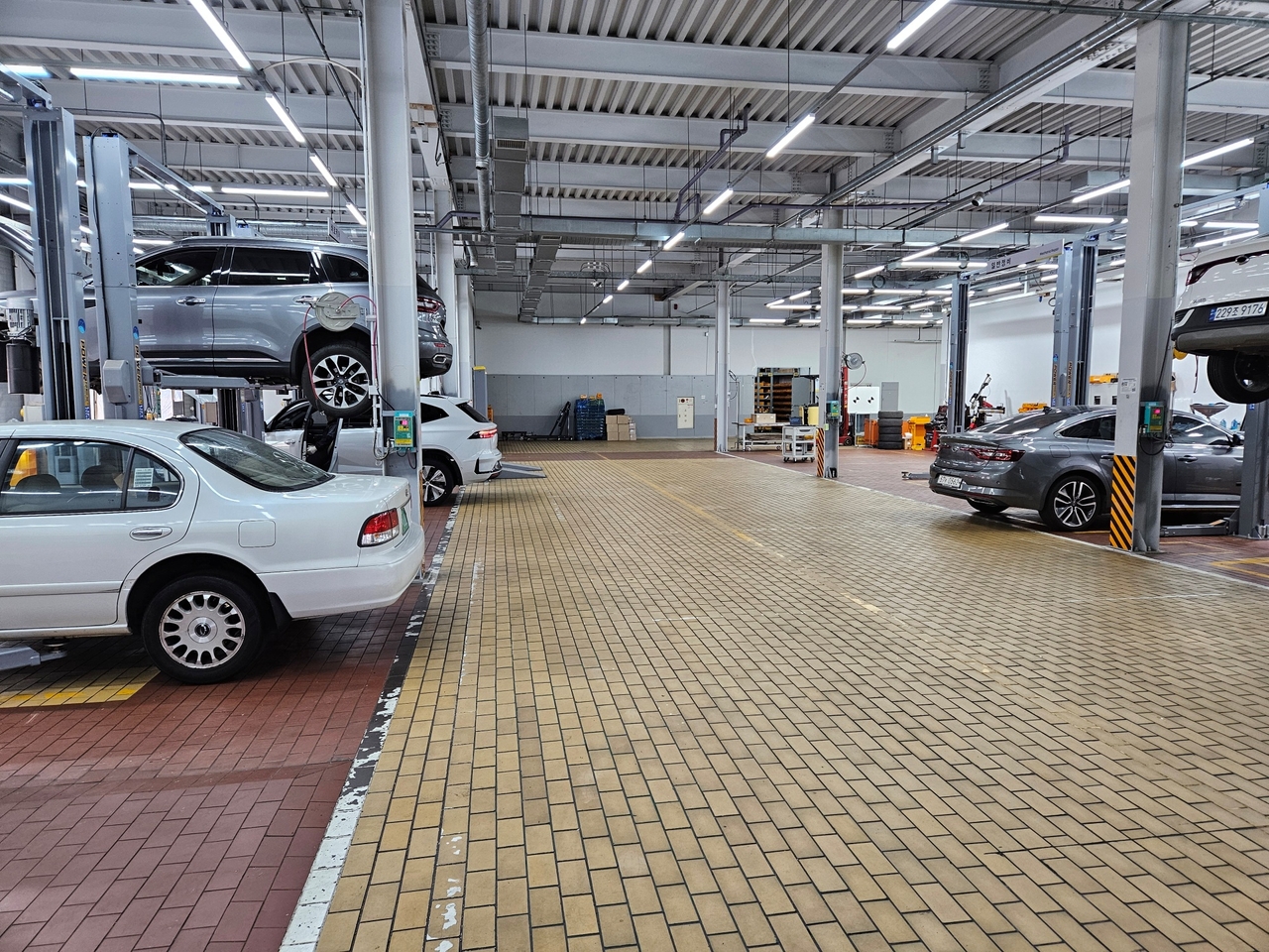 A technician inspects a vehicle in the general maintenance zone at Renault Korea's Changwon Central Service Center. The facility offers routine maintenance, warranty repairs, and servicing for electrified vehicles, including high-voltage battery work.