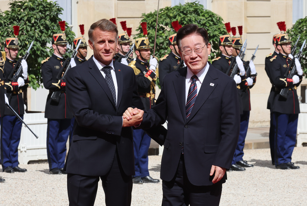 South Korean President Lee Jae Myung (R) and French President Emmanuel Macron hold hands at the Elysee Palace in Paris on Tuesday. (Yonhap)