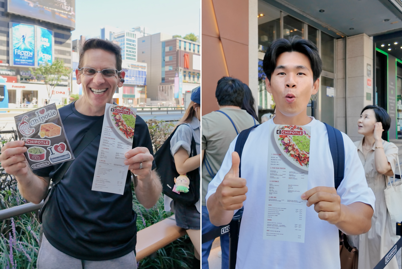 Saul Milgram (left) and Lim Chae-hwan hold up Chipotle menus and stickers handed out by staff while they wait in line. (Tammy Park/The Korea Herald)