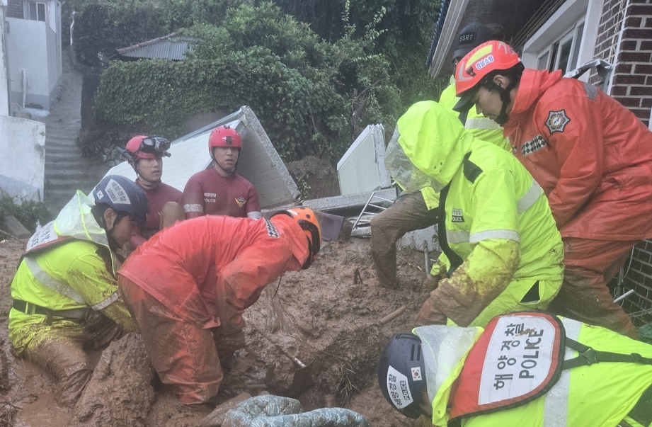 Coast Guard officers dig through earth in Tongyeong, South Gyeongsang Province, on Aug. 17, before pulling out a woman in her 60s who was buried in a landslide. (Tongyeong Coast Guard)