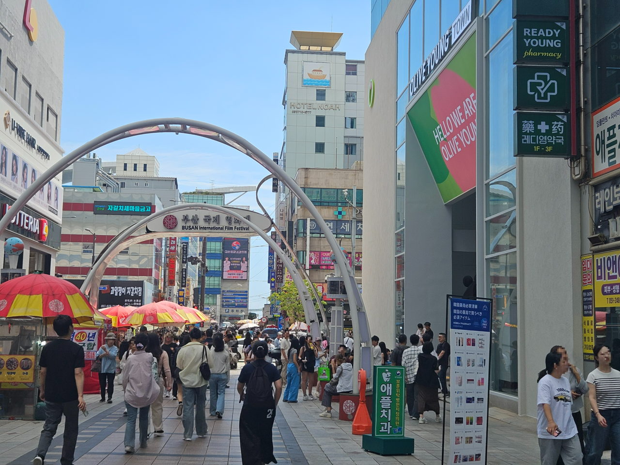 The exterior of CJ Olive Young Nampo Town on Friday. Foreign shoppers who have finished their purchases gather around benches in front of the store, while a row of street food stalls lines the opposite side of the street. A warehouse-style pharmacy recently opened right next door to Nampo Town. [Kim Jin]