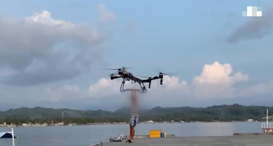 A heavy-duty drone carries Park's associate over a body of water in this footage filmed in March. (Screen captured from JTBC report)