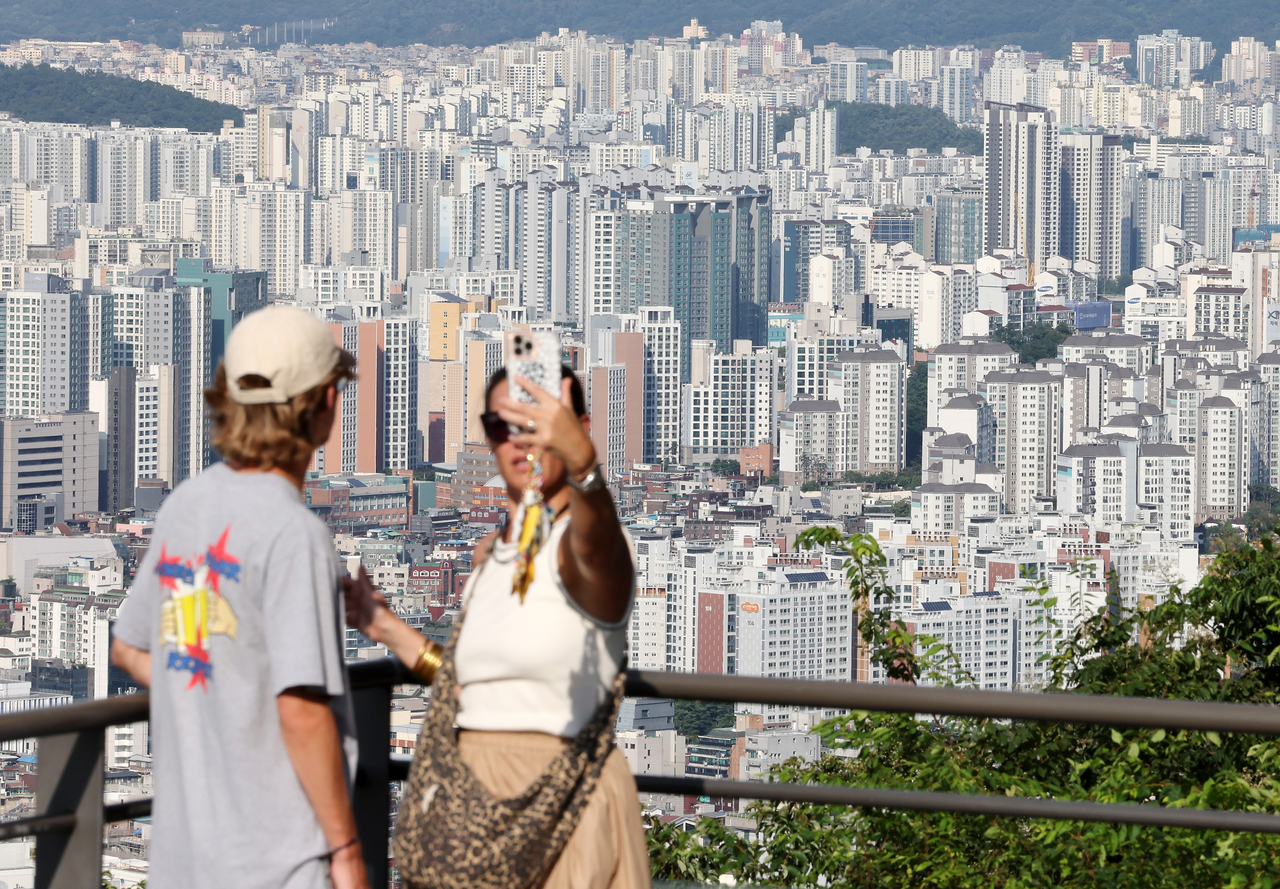 Tourists take commemorative photos against a backdrop of apartment buildings on Namsan. [Yonhap]