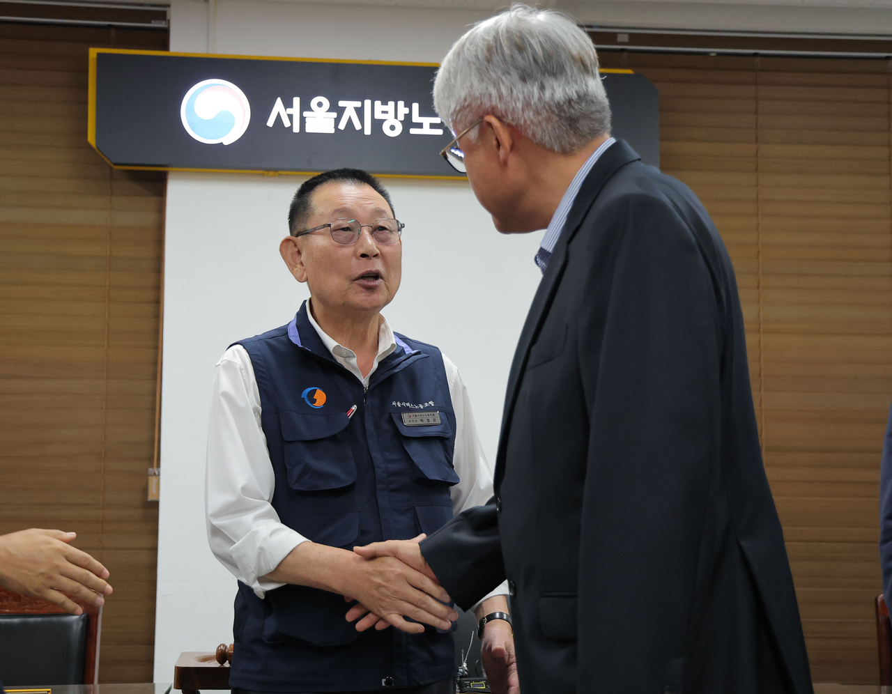 Park Jeom-gon (left), leader of the Seoul Bus Drivers Labor Union, shakes hands with Kim Jeong-hwan, head of the Seoul Bus Operators Association, at the Seoul Regional Labor Relations Committee on Wednesday. The two sides reached a last-minute agreement in the early morning to avoid an all-out strike, initially set to begin at 4 a.m. (Yonhap)