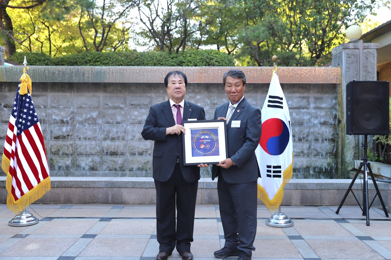 SM Group Chairman Woo Oh-hyun (left) and Korea-US Alliance Foundation President Lim Ho-young pose with the corporate supporter plaque at a sponsor meeting held at Dragon Hill Sables in Yongsan-gu, Seoul, on Wednesday. [SM Group]