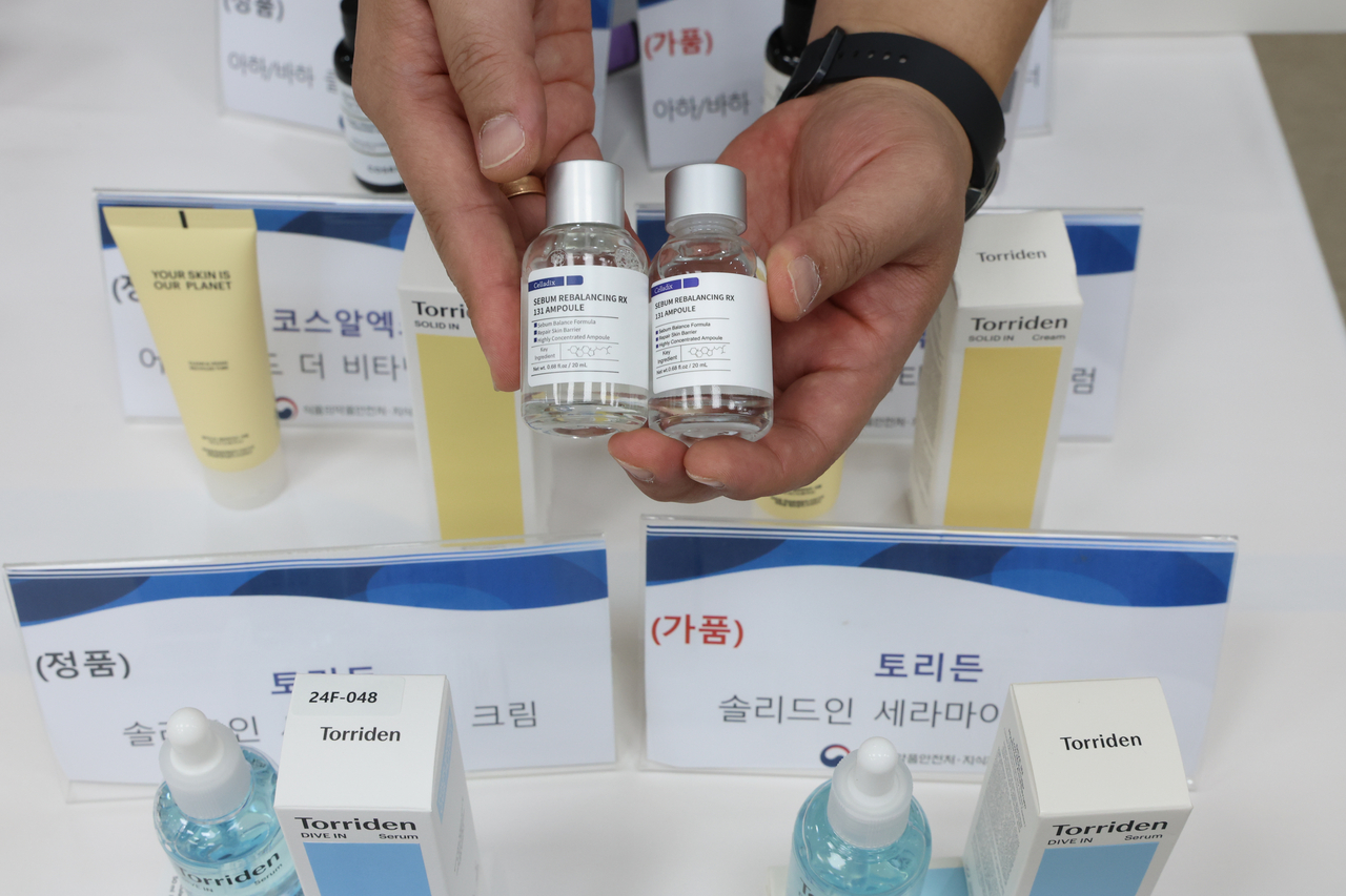 An official from the Ministry of Food and Drug Safety compares a counterfeit cosmetic product with an authentic sample during a briefing in Yangcheon-gu, Seoul, Thursday. (Yonhap)