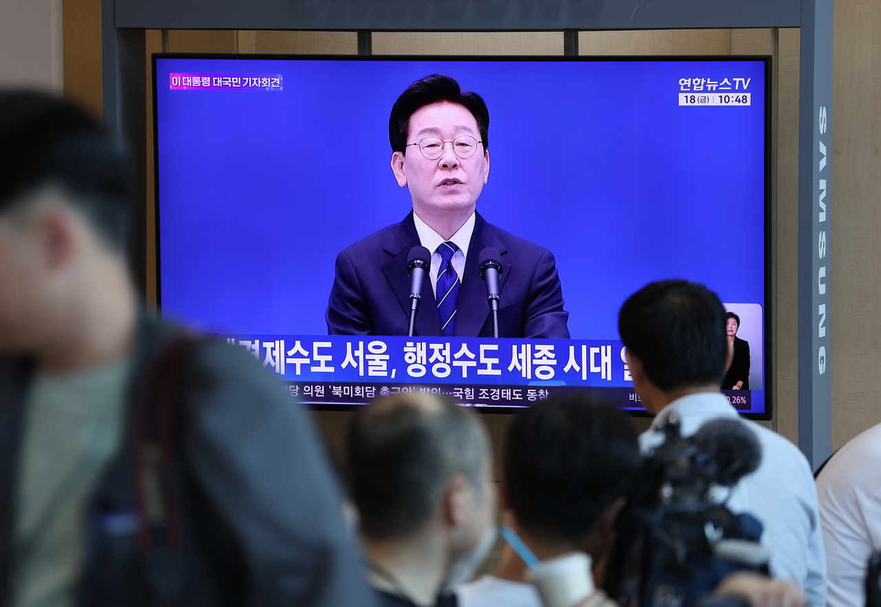 People watch a televised news conference by President Lee Jae Myung at Seoul Station on Friday. (Yonhap)