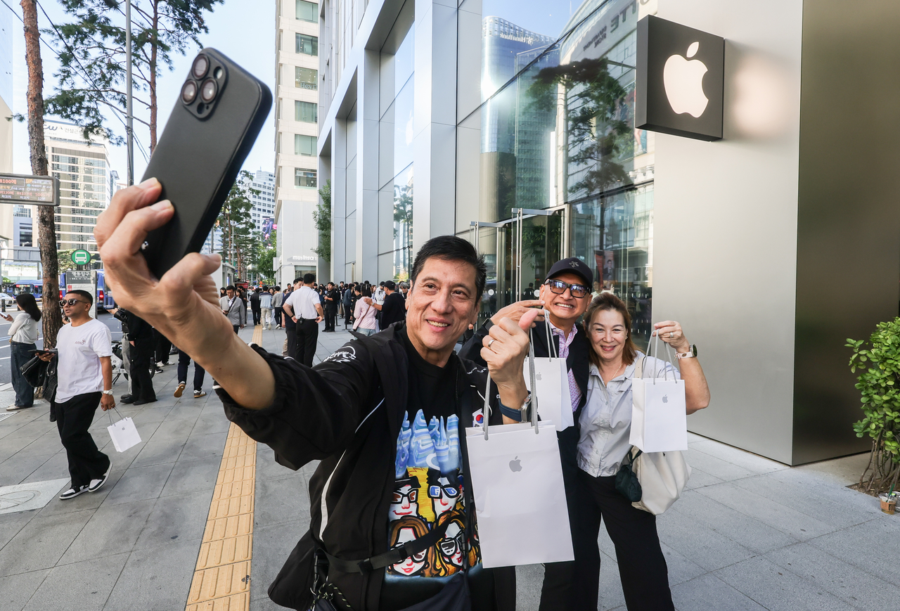 International customers take a selfie outside Apple Myeongdong in central Seoul on Friday morning after purchasing phones from the newly released iPhone 18 series. (Yoon Chang-bin/The Korea Herald)
