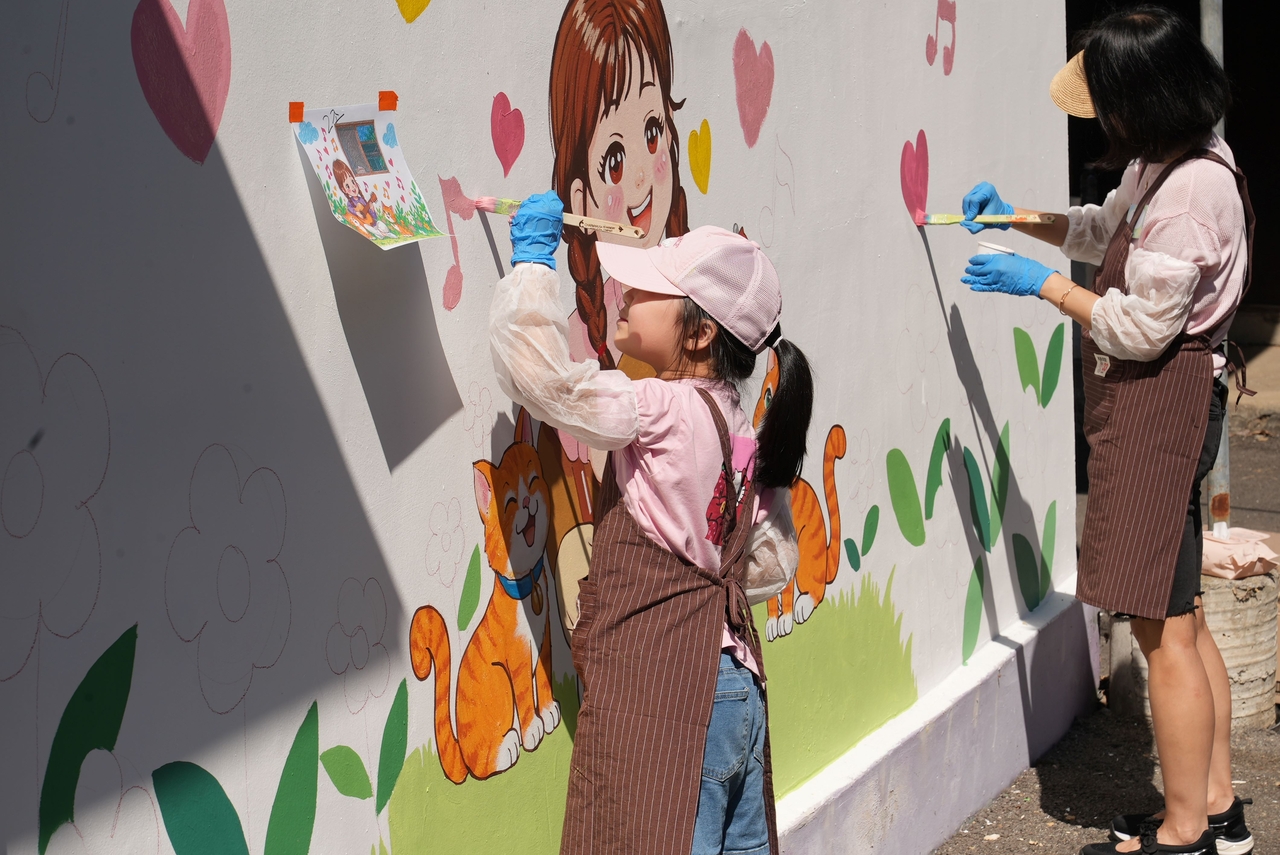 A young volunteer paints a mural at Yeonpung Village in Paju, Gyeonggi Province, during a "Sharing Happiness Mural Painting" volunteer event on Saturday. [Provided by Korea Investment & Securities]