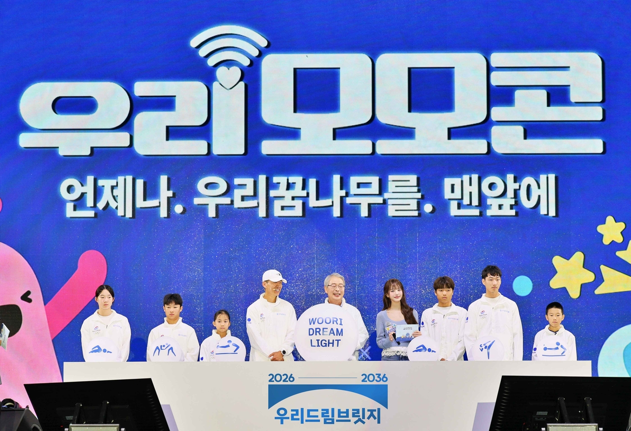 Woori Financial Group Chairman Lim Jong-ryong (fifth from left), Woori Bank brand ambassador and singer Jang Won-young (fourth from right), and singer Shawn (fourth from left) pose with athletes supported by the Woori Dream Bridge program at the 2026 Woori MomoCon at Seoul Land in Gwacheon on Saturday, where the group officially launched its Woori Dream Bridge sports social contribution initiative. [Woori Financial Group]